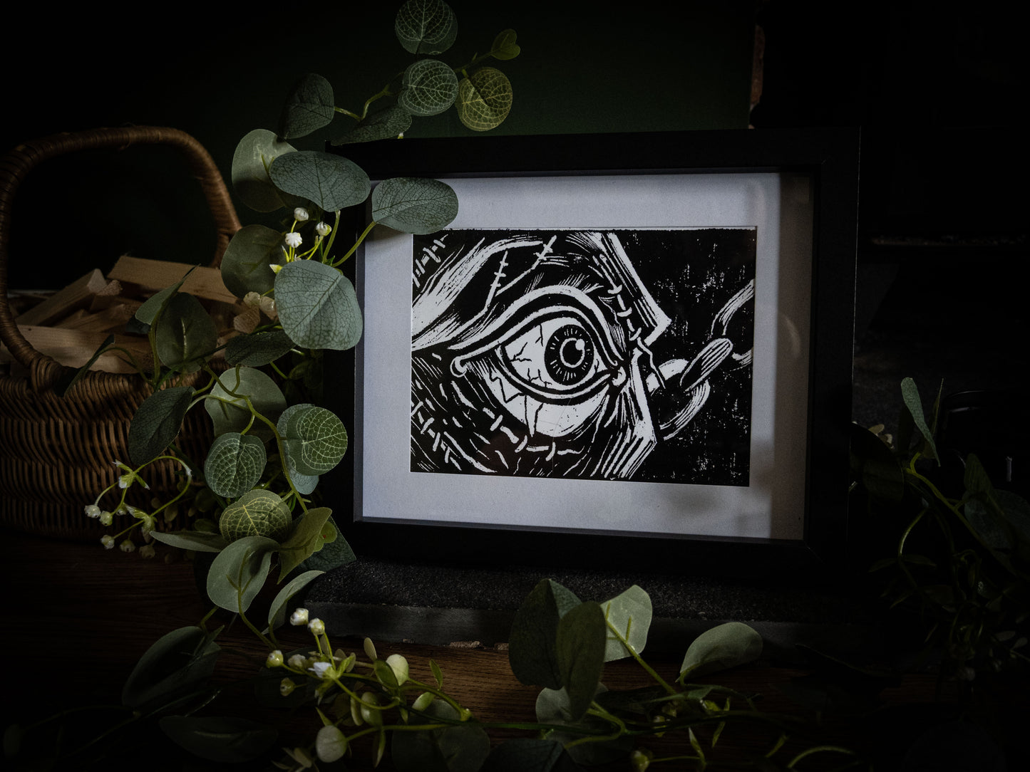 The First Sight art print with wicker basket and eucalyptus — the creature's first sight, stitched eye in extreme close-up, gothic illustration by Sophie Atkinson