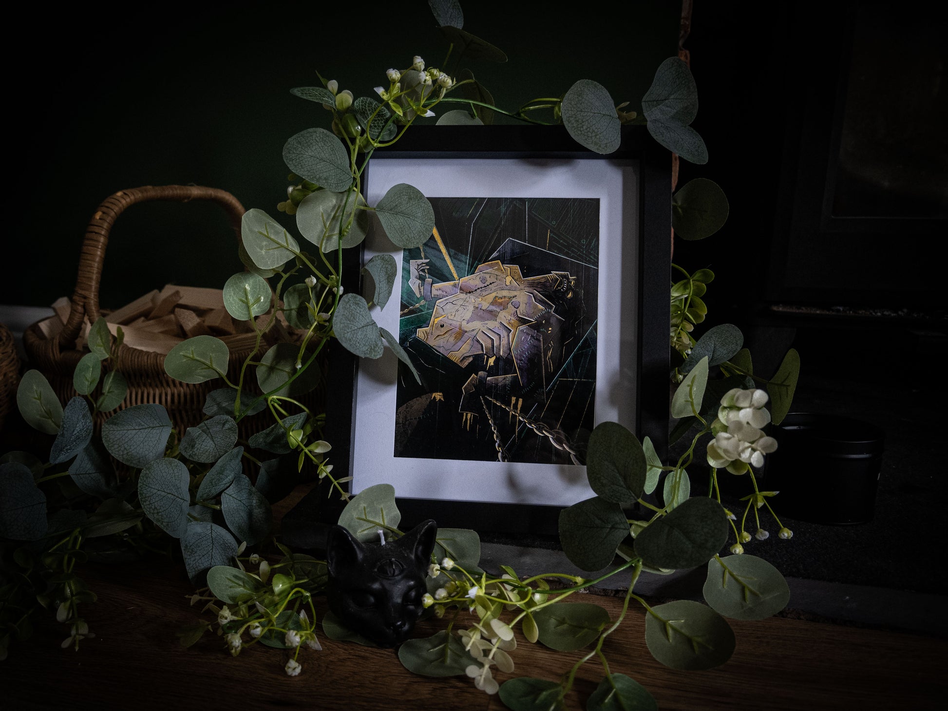 The Creature Awakens Frankenstein gothic art print by Sophie Atkinson, framed in black on a dark wooden surface surrounded by eucalyptus and foliage