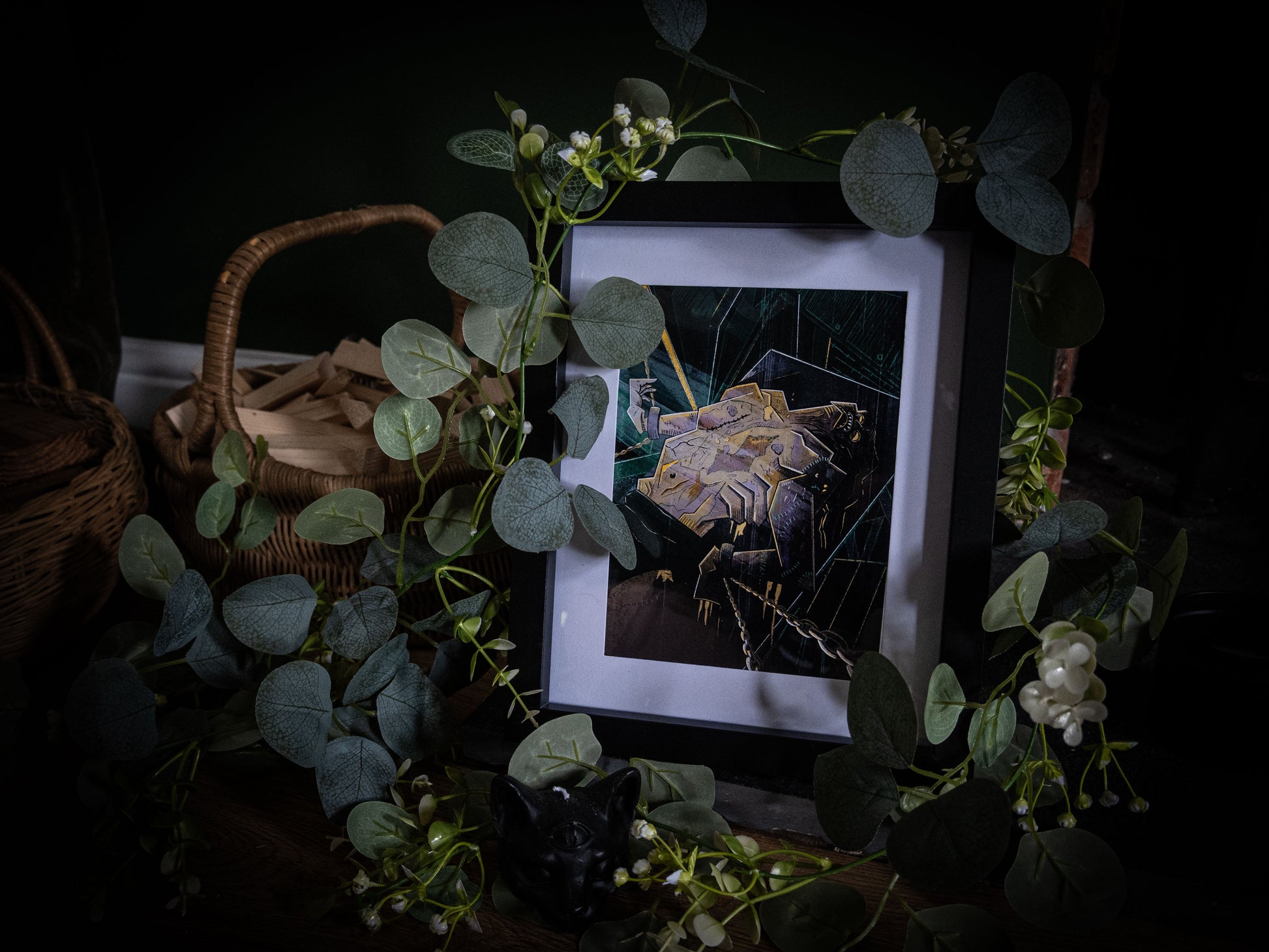 Full styled shot of The Creature Awakens Frankenstein print in black frame, eucalyptus garland and wicker basket on dark wooden surface