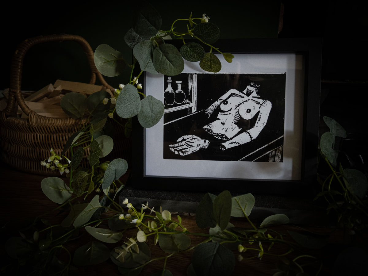 Close-up of The Workshop art print — stitched creature on workbench with skeletal hand, high-contrast gothic illustration