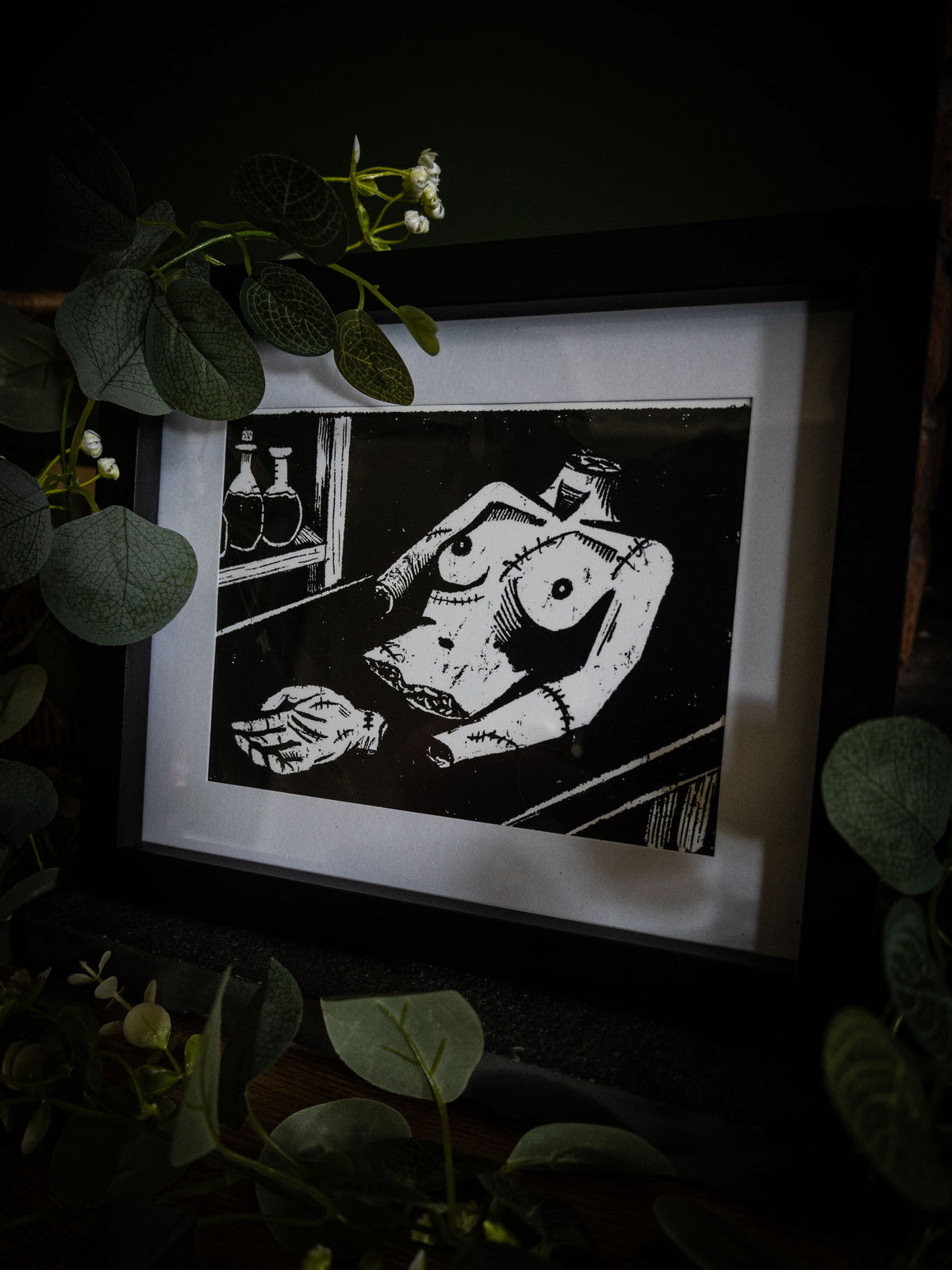 The Workshop art print in black frame with wicker basket — bold gothic illustration of the creature before creation, by Sophie Atkinson