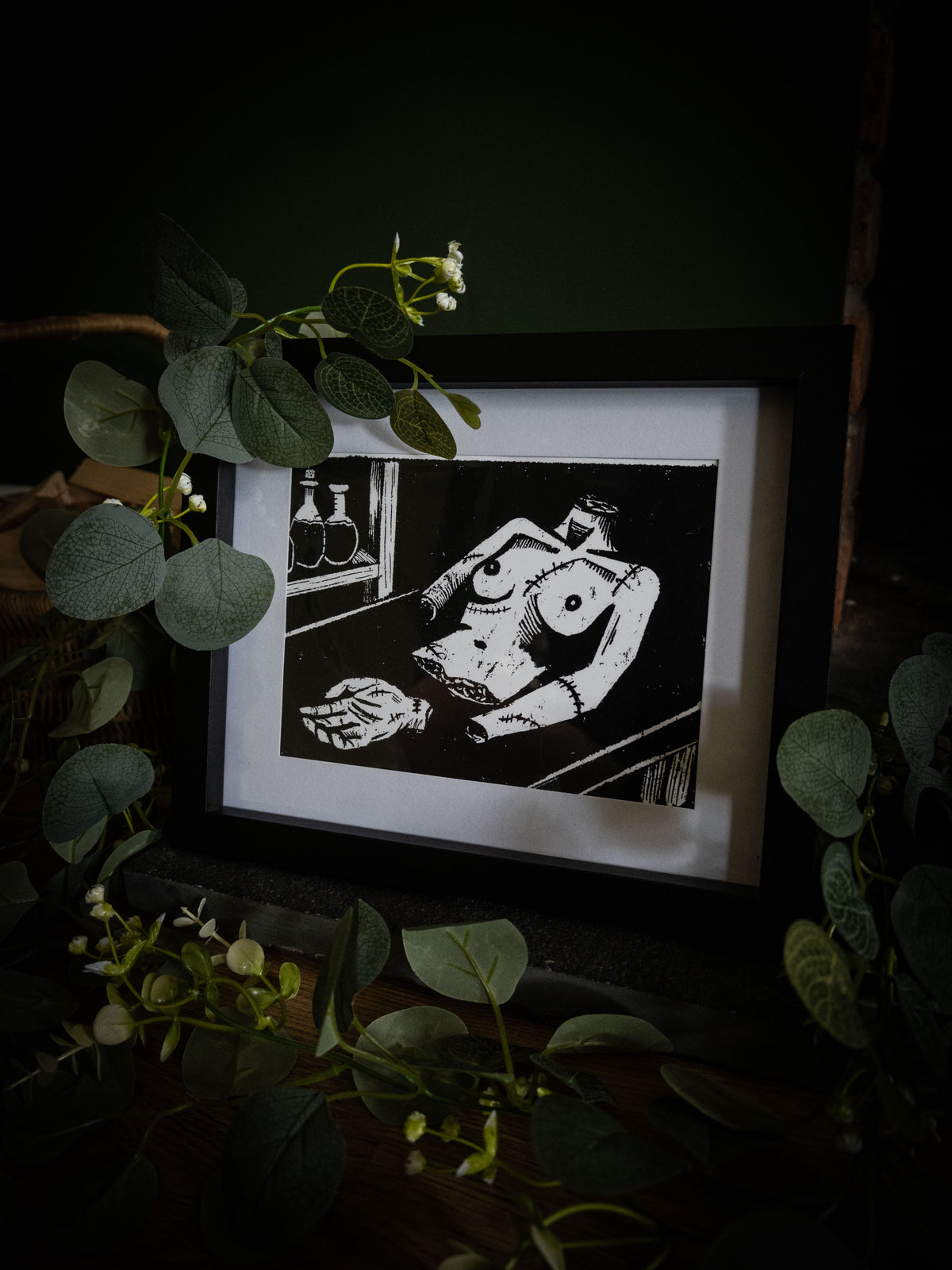 Framed gothic art print of Frankenstein's creature on the workbench, stitched limbs and potion bottles, from Sophie Atkinson's Frankenstein Illustrated series