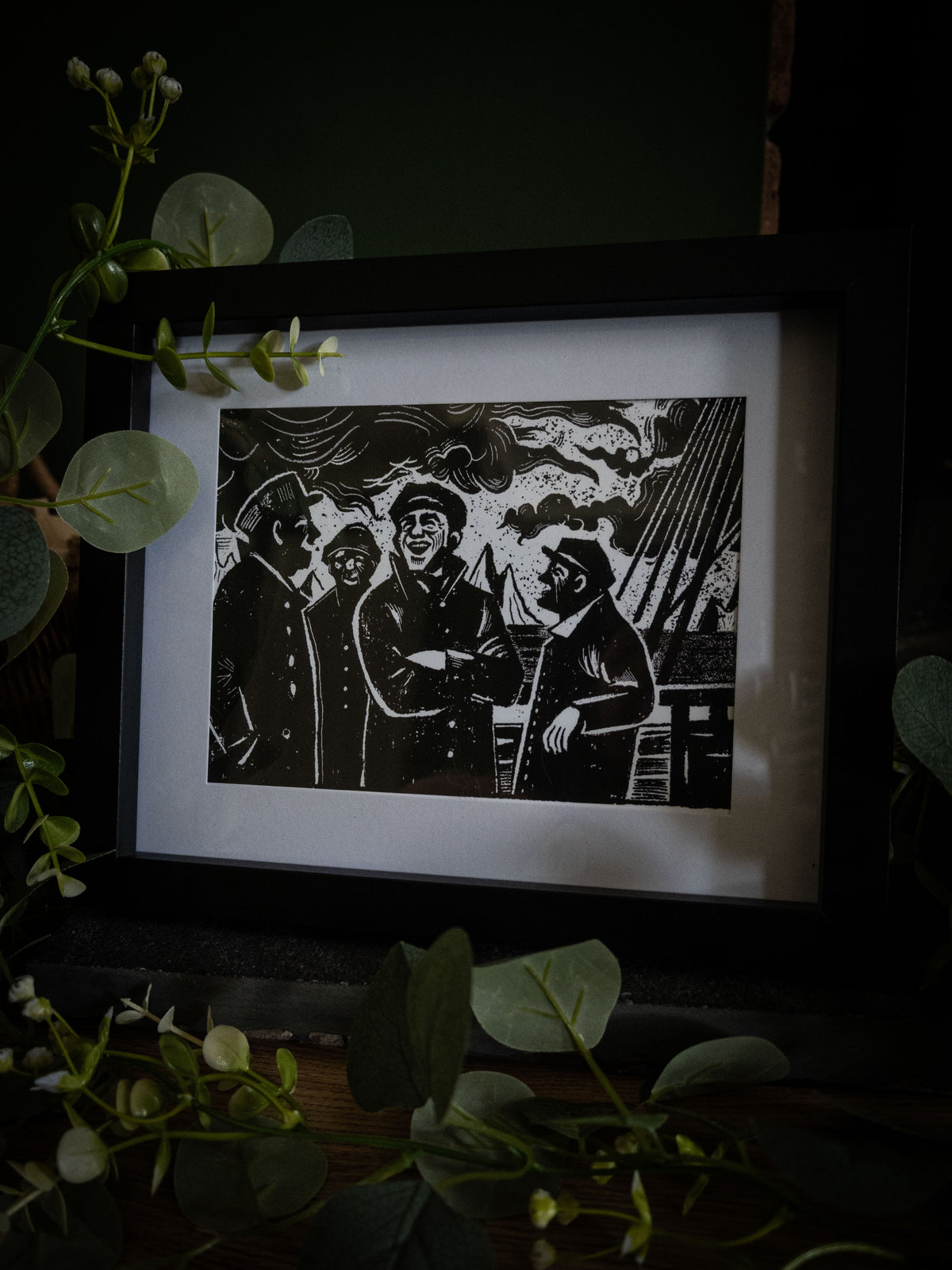 The Voyage art print in black frame with wicker basket — sailors on deck in stormy weather, bold gothic illustration by Sophie Atkinson