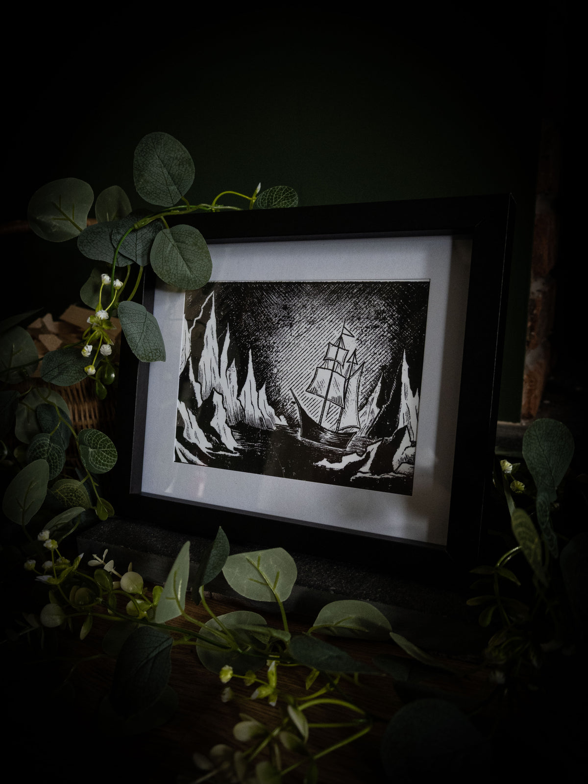The Arctic art print in black frame with eucalyptus — sailing ship among towering icebergs, bold gothic illustration by Sophie Atkinson