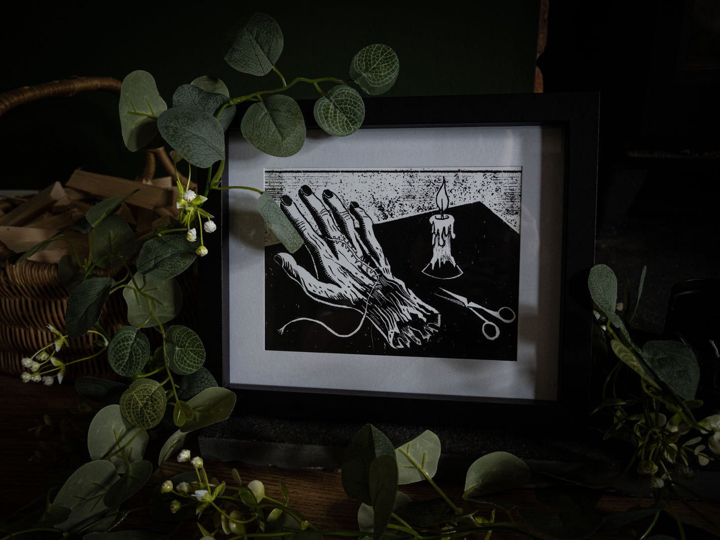 The Stitching art print wide shot with wicker basket and eucalyptus — stitched hand on workbench by candlelight, gothic illustration by Sophie Atkinson