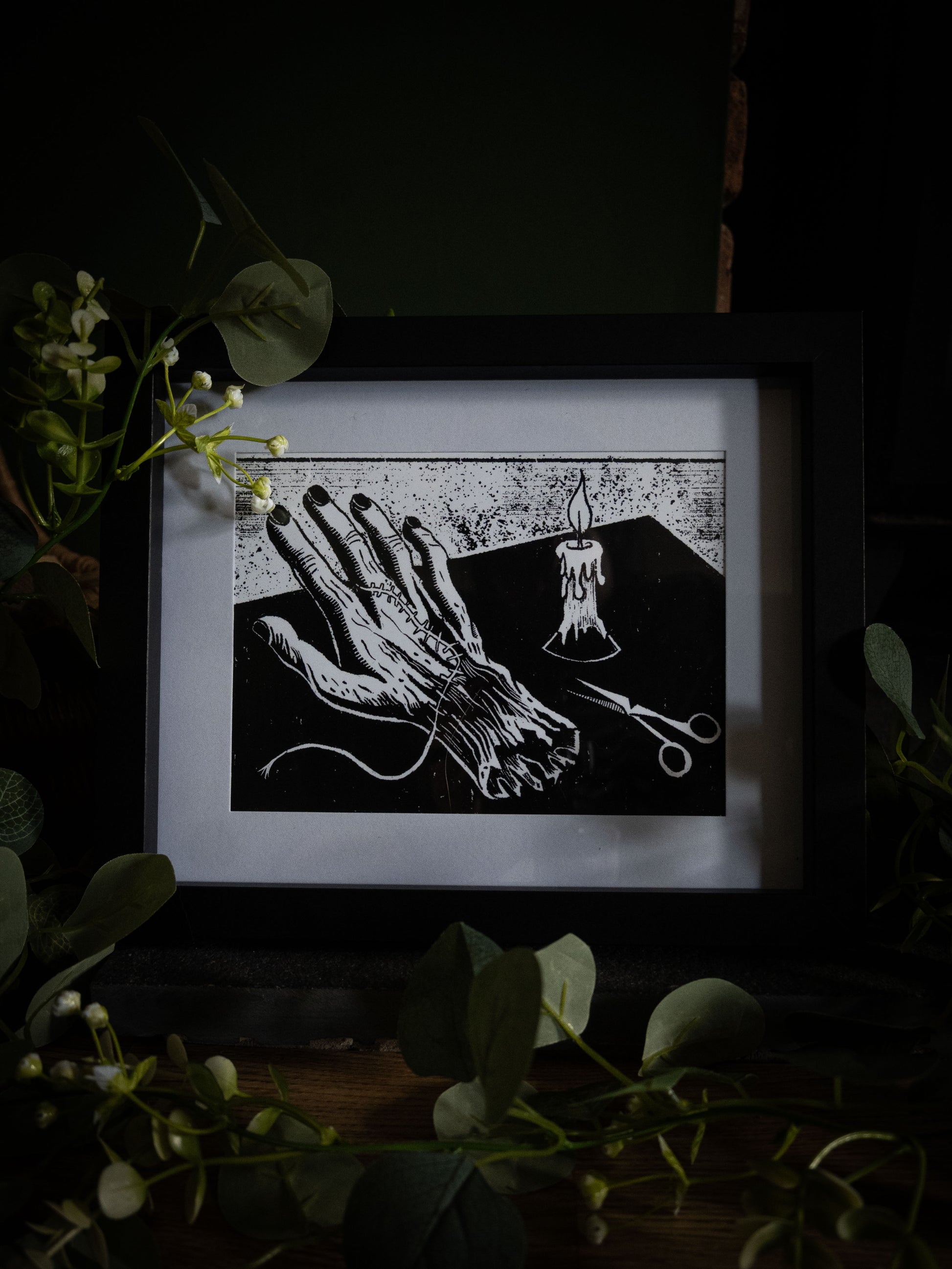 Framed gothic art print of the creature's stitched hand on a workbench by candlelight, from Sophie Atkinson's Frankenstein Illustrated series