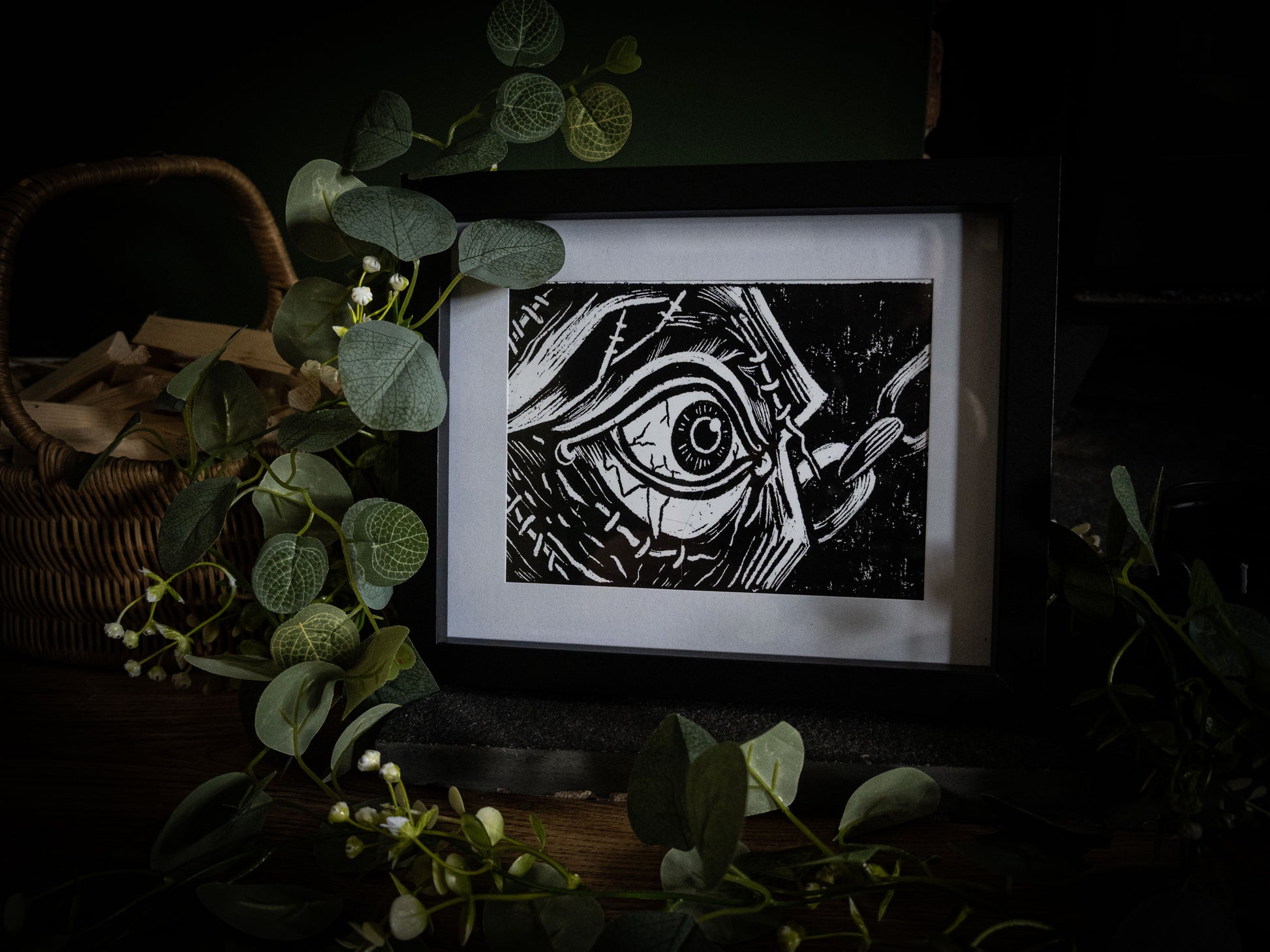 The First Sight art print with wicker basket and eucalyptus — the creature's first sight, stitched eye in extreme close-up, gothic illustration by Sophie Atkinson