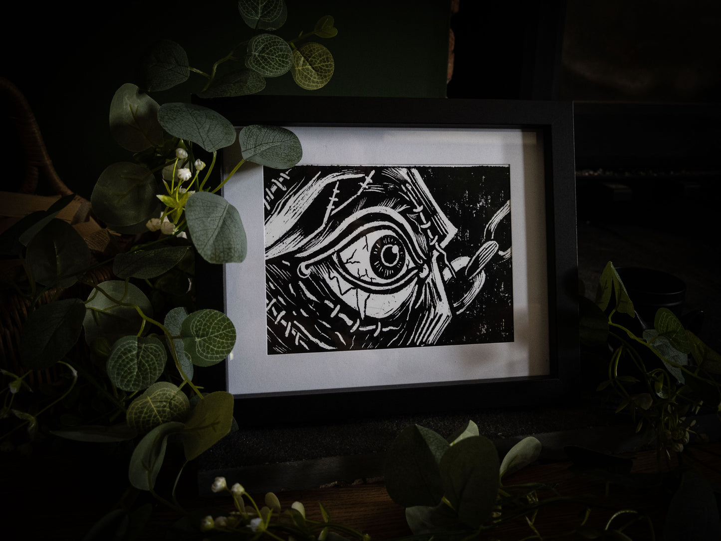The First Sight giclée print displayed with winter foliage — Frankenstein creature's eye opening, stitched skin close-up, gothic artwork