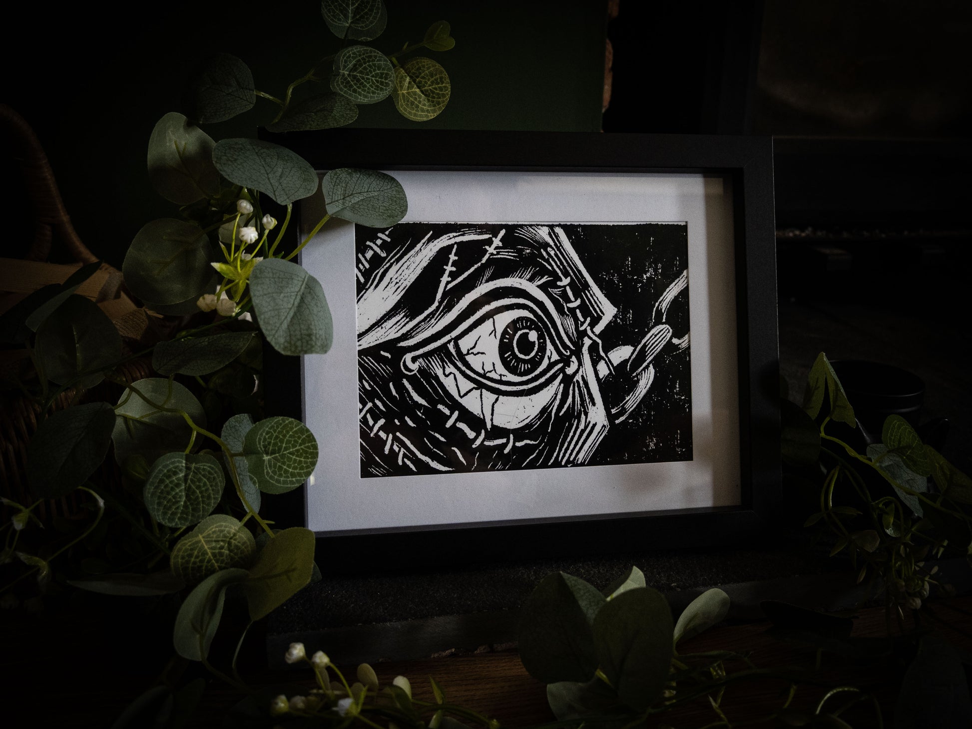 The First Sight giclée print displayed with winter foliage — Frankenstein creature's eye opening, stitched skin close-up, gothic artwork