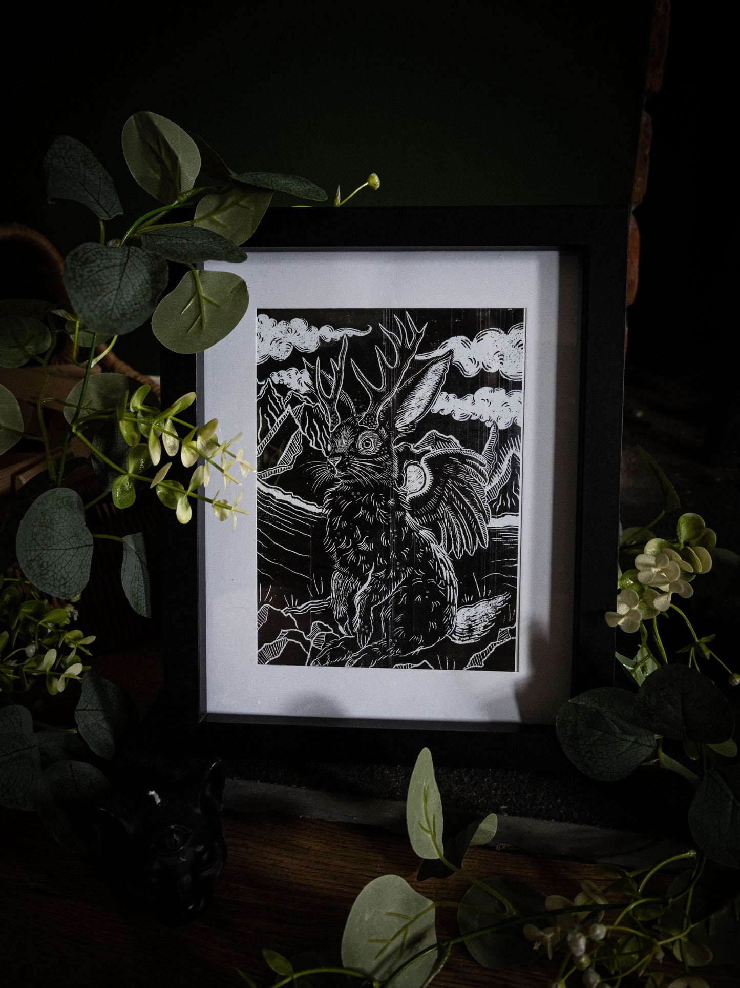 Gothic Jackalope fine art print framed and styled with dark florals and eucalyptus on a wooden surface