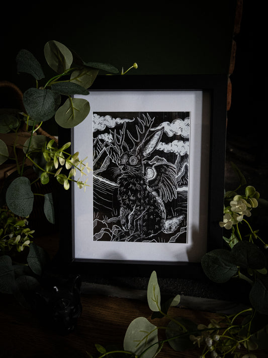 Gothic Jackalope fine art print framed and styled with dark florals and eucalyptus on a wooden surface