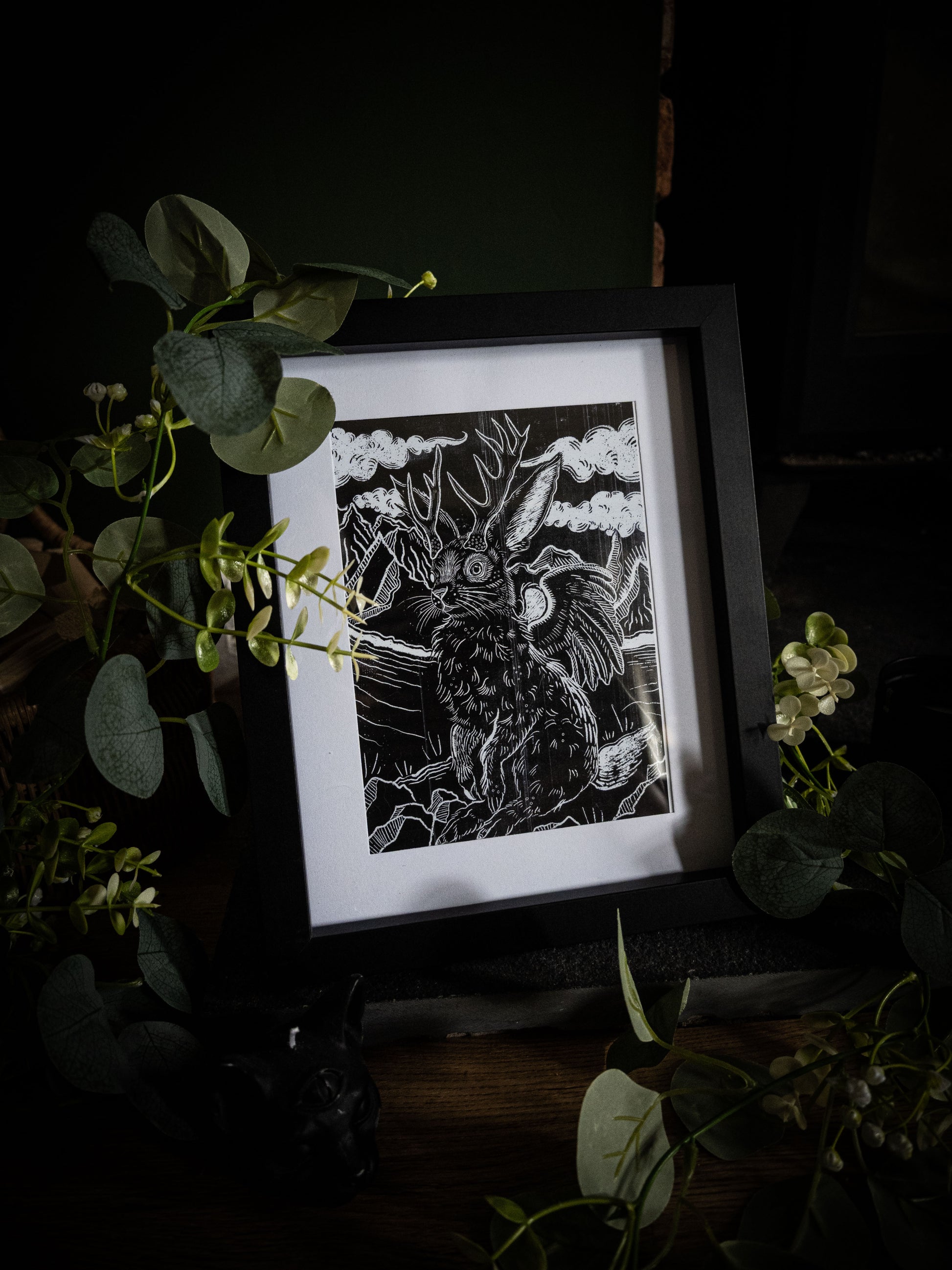Jackalope creature art print by Sophie Atkinson in black frame, dark background with trailing foliage and white flowers