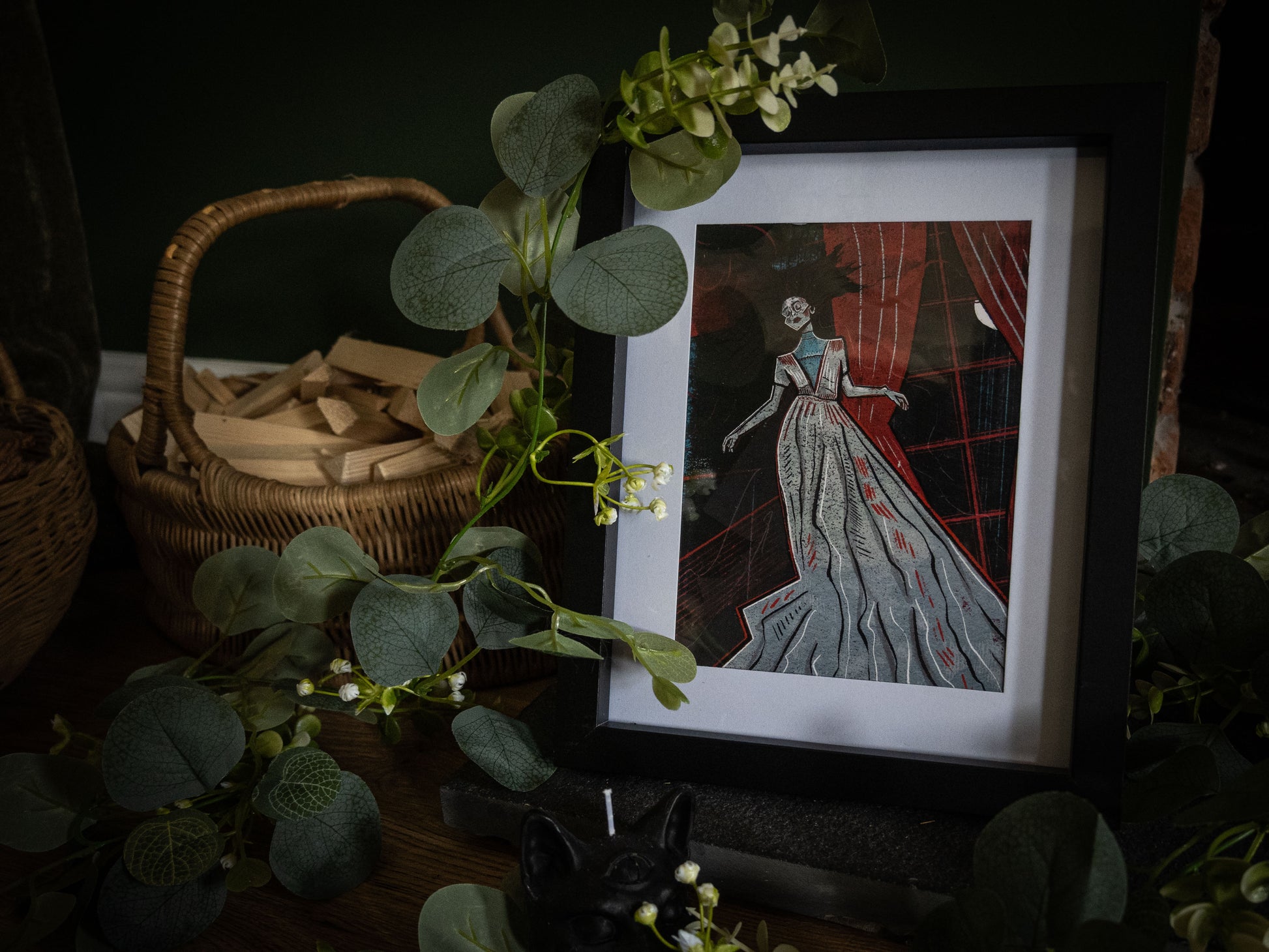 The Lady Ligeia gothic art print in black frame – spectral woman in grey gown against crimson curtains, styled with eucalyptus and wicker basket