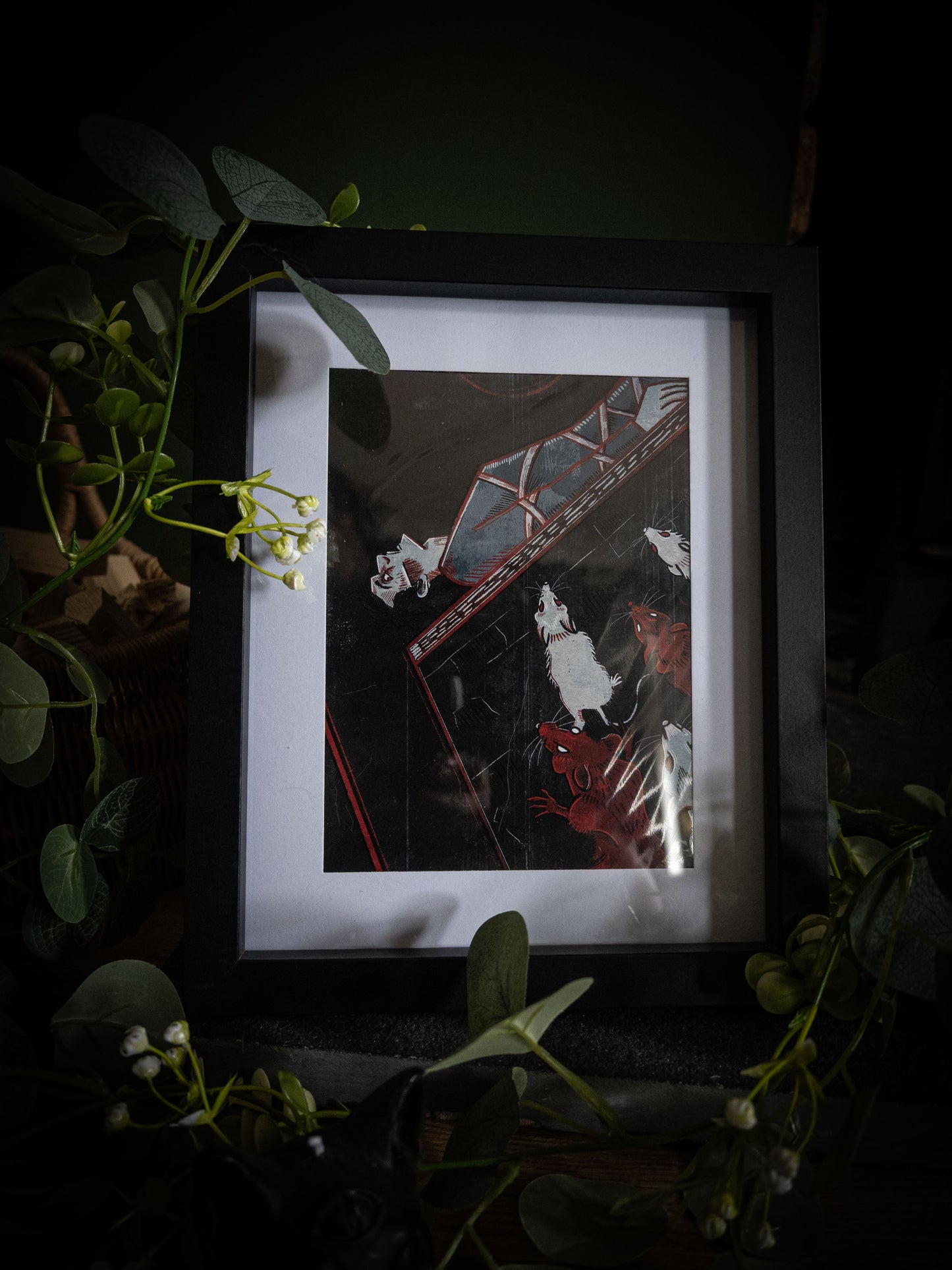 Close-up of The Pit and the Pendulum illustration print in black frame, bold woodblock-style artwork with swinging pendulum and swarming rats, styled with botanical foliage