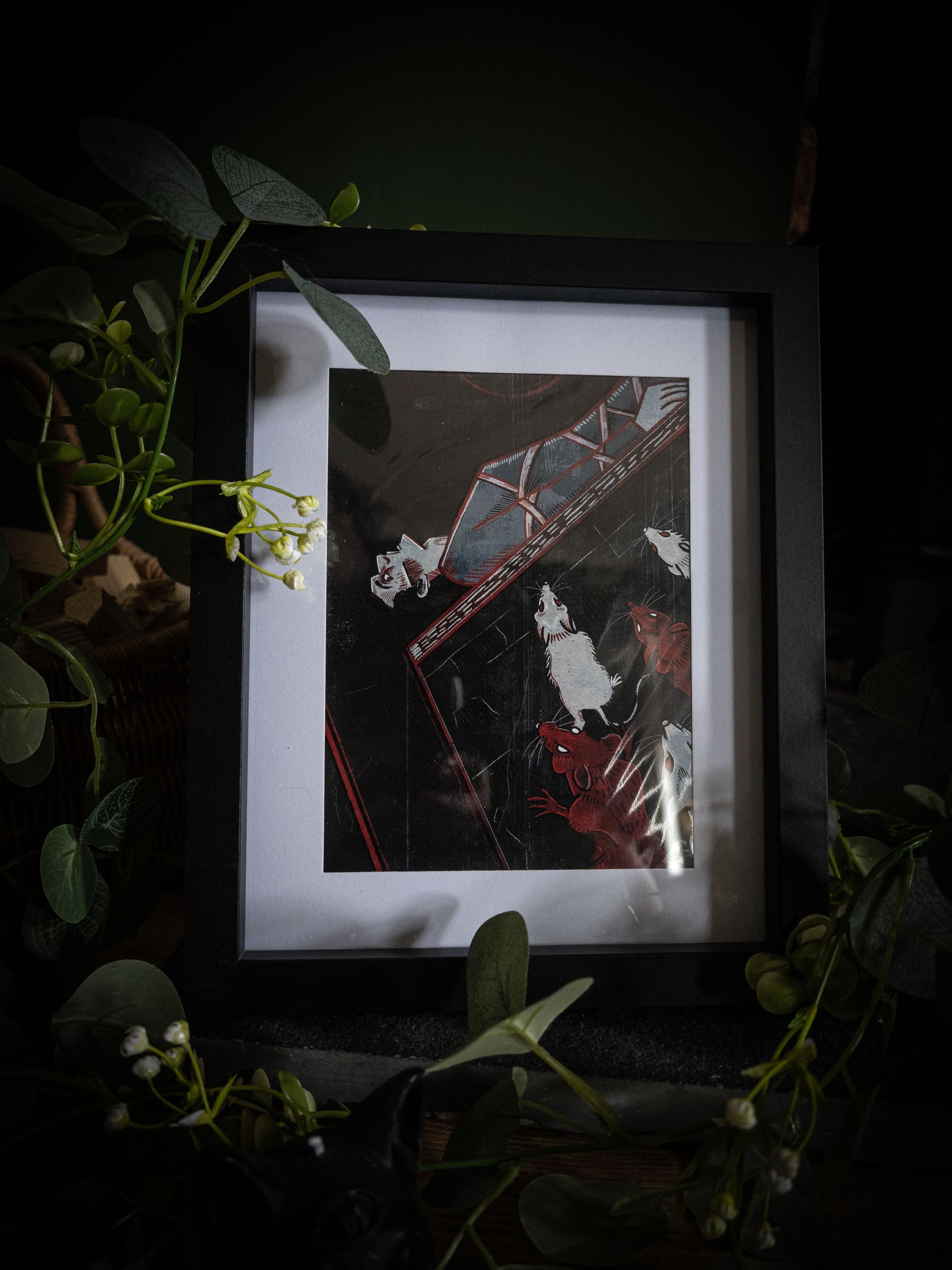 Close-up of The Pit and the Pendulum illustration print in black frame, bold woodblock-style artwork with swinging pendulum and swarming rats, styled with botanical foliage