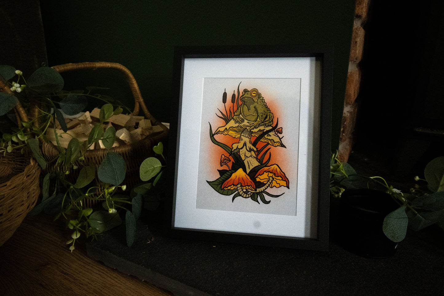 Witch's Familiar giclée print in black frame displayed on dark wooden surface with eucalyptus