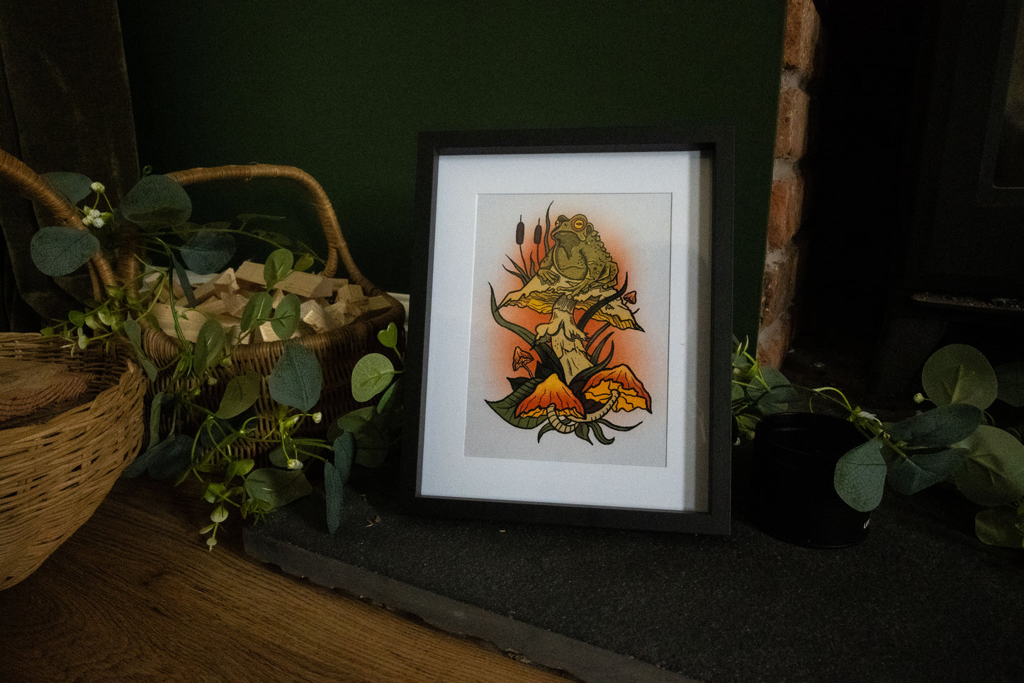 Witch's Familiar toad print framed in black, atmospheric dark setting with basket and plants