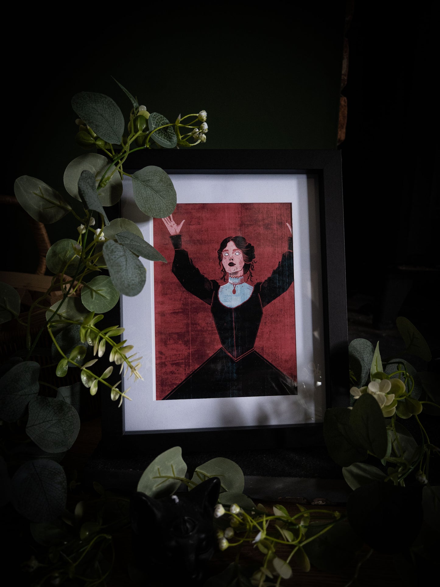 Mina Harker gothic fine art print by Sophie Atkinson in black frame, angled view surrounded by eucalyptus and white flowers on dark surface