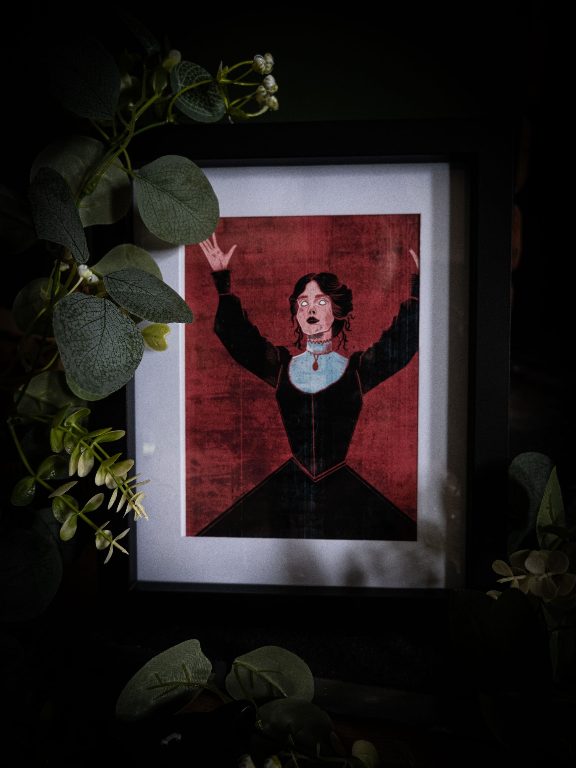 Mina Harker illustrated book art print in black frame, moody dark background with botanical props, figure with arms raised in dramatic pose