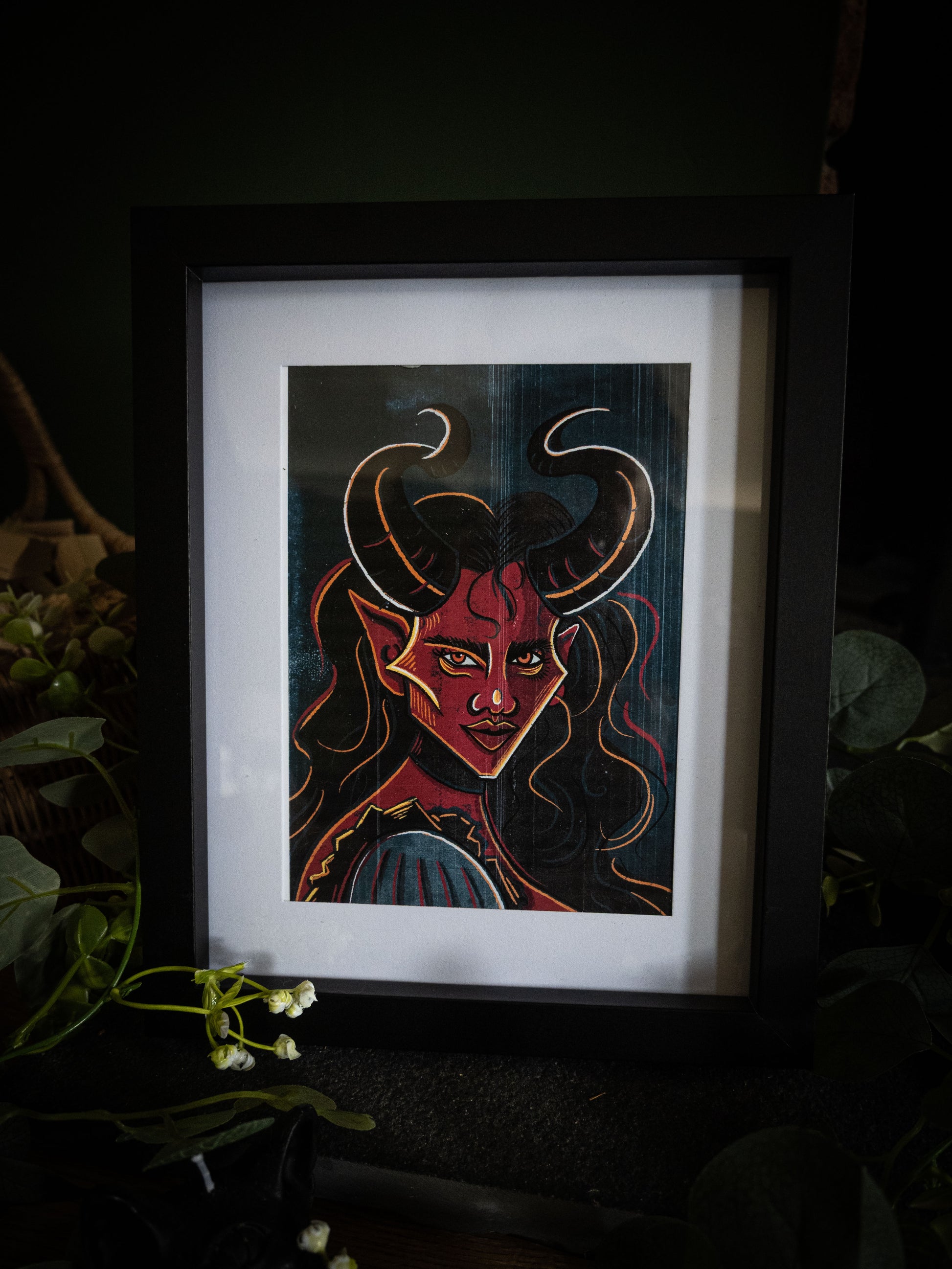 The Horned Temptress fine art print in black frame – crimson demoness with sweeping horns, dark moody product photography