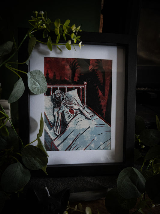 Full view of The Tell-Tale Heart gothic art print in black frame, styled with trailing eucalyptus and white blooms on dark surface near window light