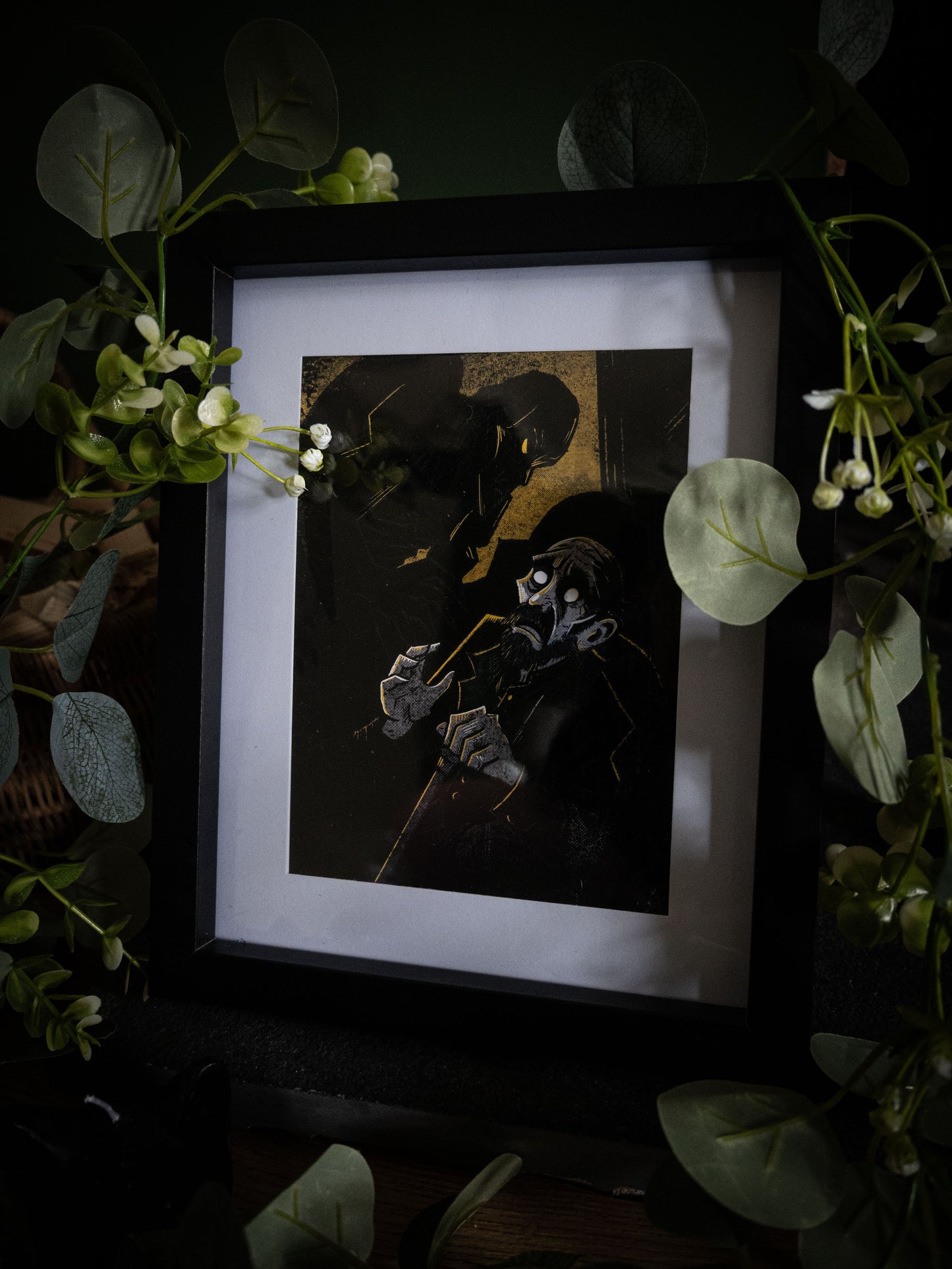 The Blind Man art print in black frame with trailing foliage — De Lacey hollow-eyed with vast shadow, bold gothic illustration by Sophie Atkinson