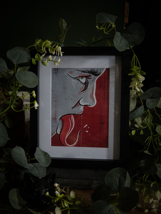 Speak No Evil art print in black frame – dramatic red and grey linocut face profile with dark botanical styling