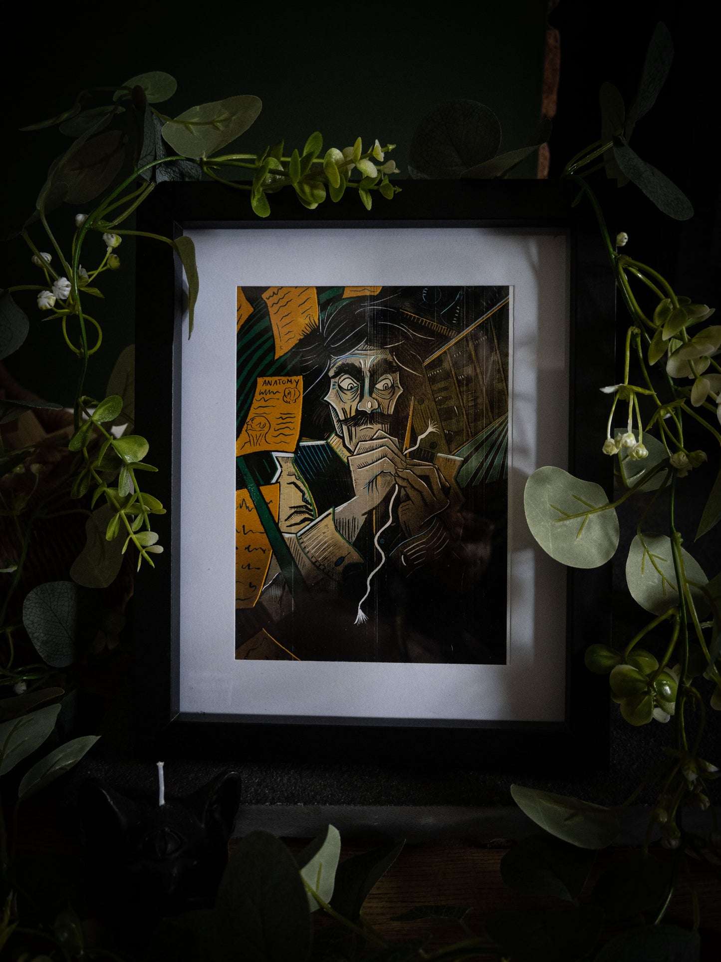 Victor art print in black frame with trailing foliage — Victor Frankenstein hunched over his creation, amber and teal colour illustration by Sophie Atkinson