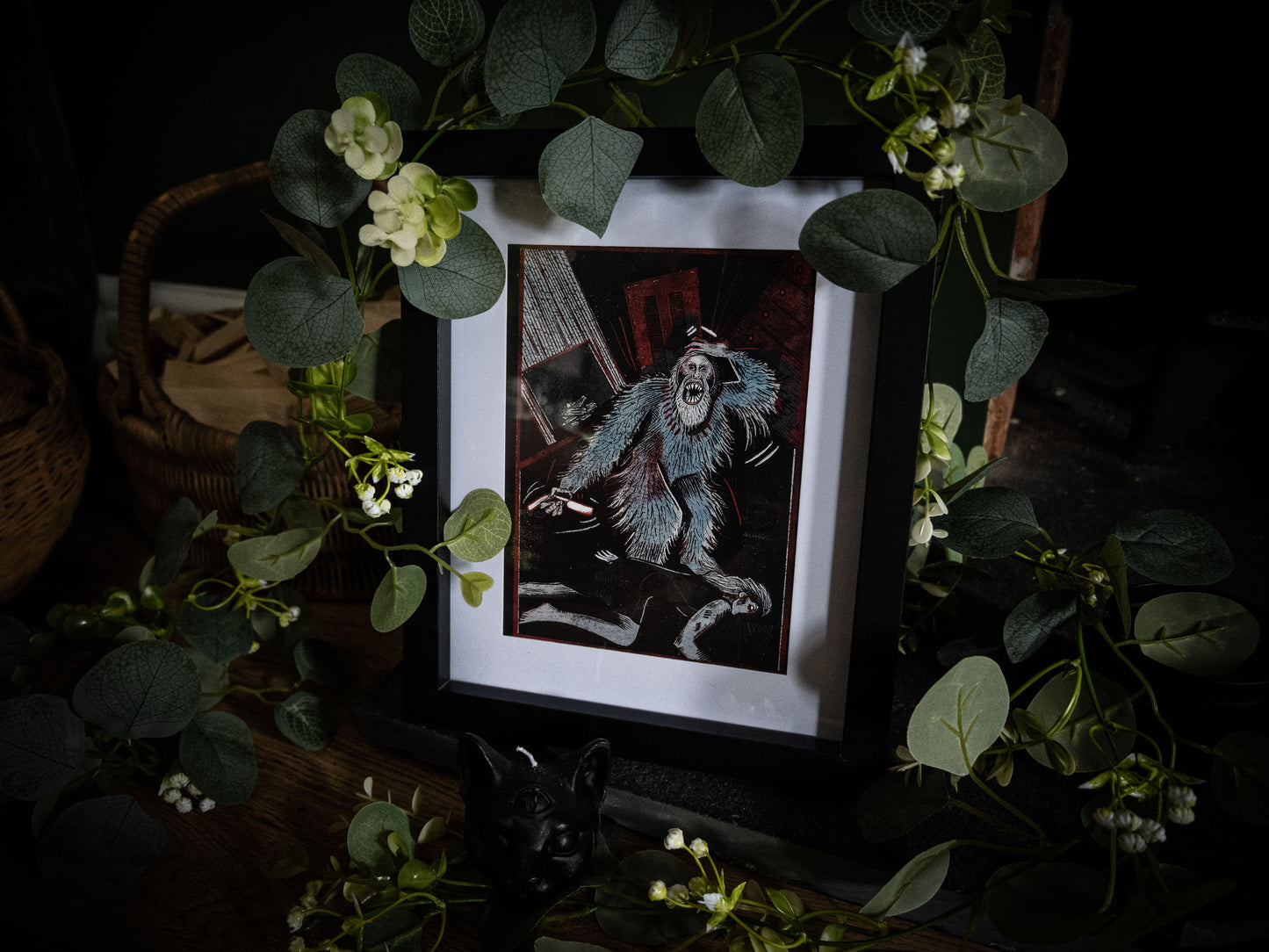 The Murders in the Rue Morgue gothic art print by Sophie Atkinson, framed in black surrounded by eucalyptus and white flowers, showing the orangutan creature in teal and crimson woodblock style