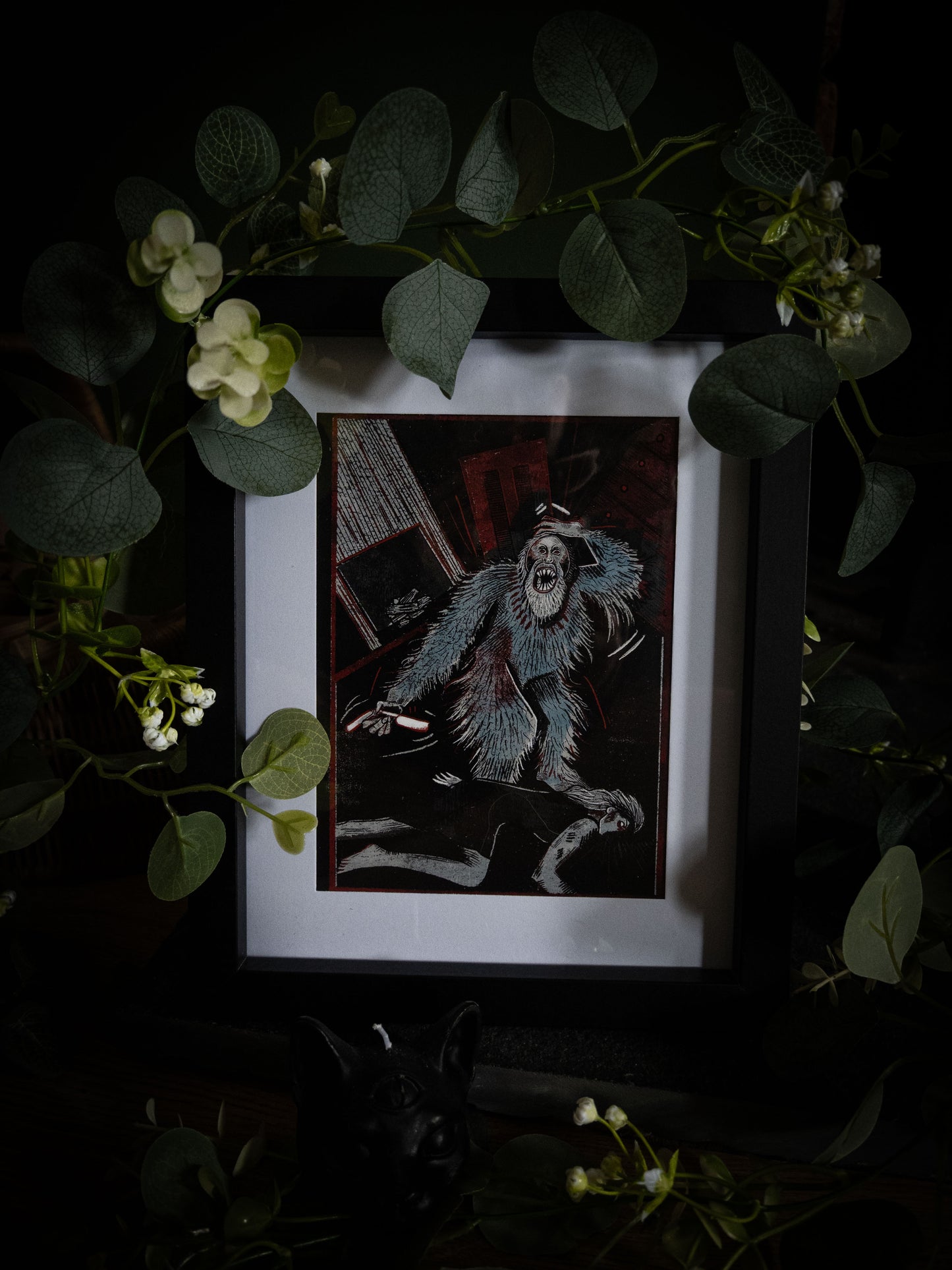 Close-up of Murders in the Rue Morgue illustration print in black frame, bold woodblock-style artwork of rampaging creature in deep teal and black with crimson accents, styled with botanical foliage