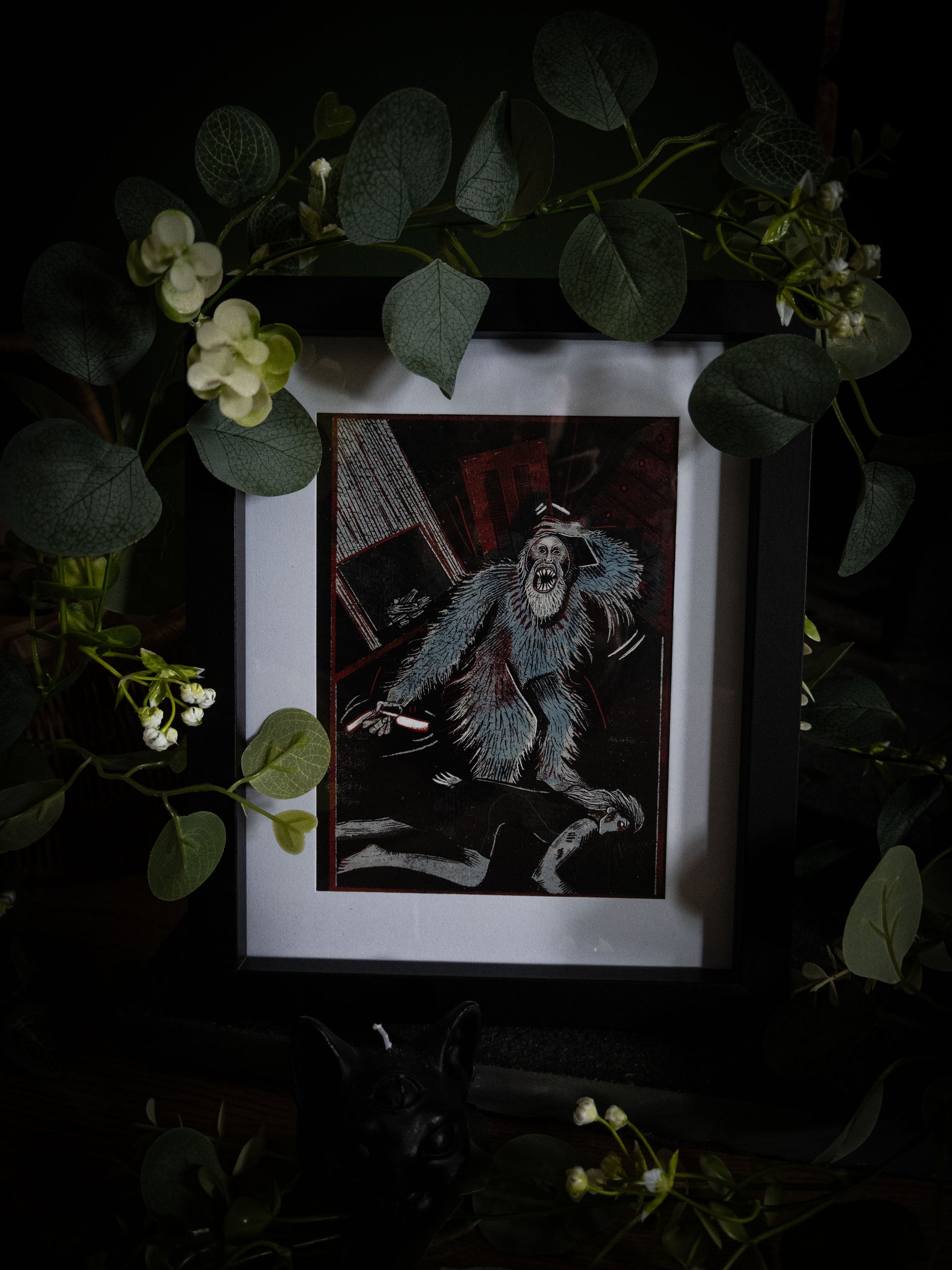 Close-up of Murders in the Rue Morgue illustration print in black frame, bold woodblock-style artwork of rampaging creature in deep teal and black with crimson accents, styled with botanical foliage